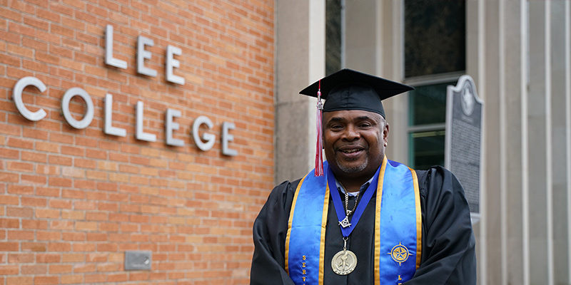 Charles Brantley stands in cap and gown before the name Lee College on a building exterior