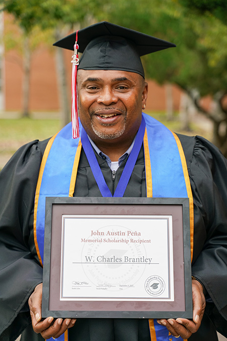 Charles Brantley in cap and gown holds his framed scholarship