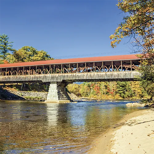 Covered railroad bridge over a river. Trees on the banks show fall colors.